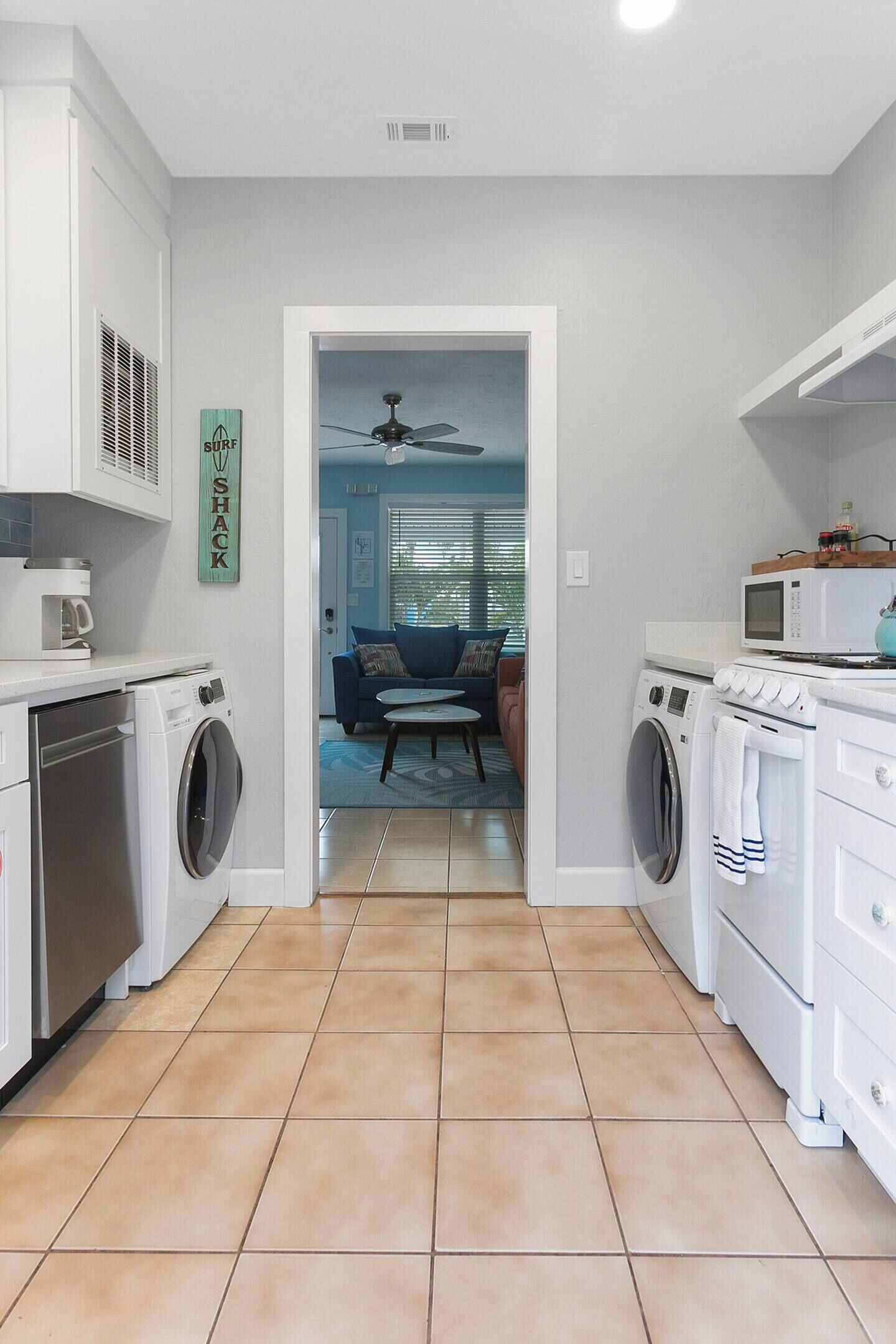 A compact kitchen with built-in appliances, a dining area with a ceiling fan, and a view into a living room with a couch and a coffee table.