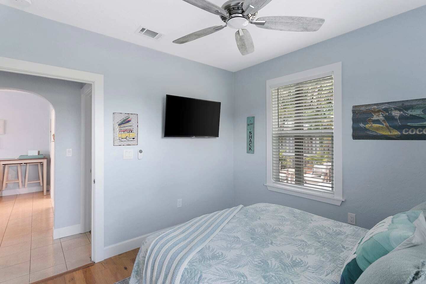 A bedroom with a bed, a ceiling fan, a TV, and a window with blinds.