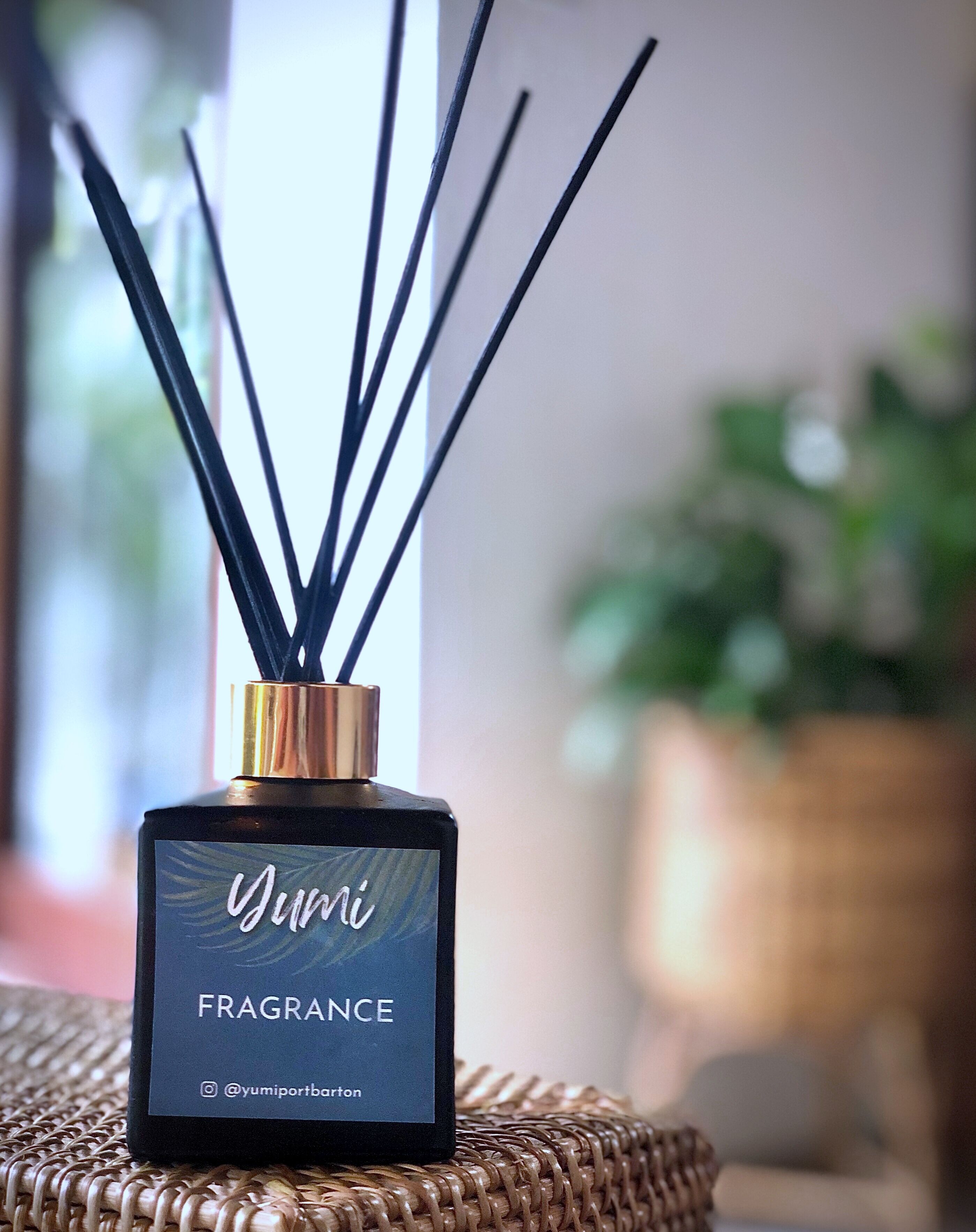 A black bottle with gold accents labeled "Yumi Fragrance" on a woven surface.