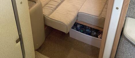 Un espacio compacto para dormir, de color beige, con una cama tipo banco, un compartimento para guardar cosas debajo y una rejilla en el techo.