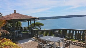 A gazebo with a tiled roof overlooking a lake, surrounded by a wooden deck with outdoor seating. - Breathtaking Clifftop Ocean Views in Eden - Unit 12 Bob and Zita’s escape (Eden)