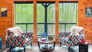A cabin interior with a large window, two patterned armchairs, a small table, and a sign reading "BASECAMPELLIJAY". - North GA Relaxing Chic Cabin w/ Resort Amenities (Ellijay)