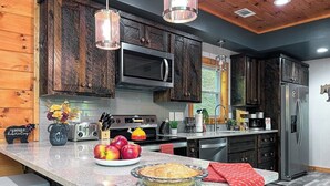A modern kitchen with dark wooden cabinets, stainless steel appliances, and a granite countertop. - North GA Relaxing Chic Cabin w/ Resort Amenities (Ellijay)