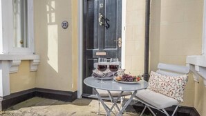 A small outdoor seating area with a table and chairs, a door with the number 12, and a window to the left. - No 12. Southwold (Southwold)