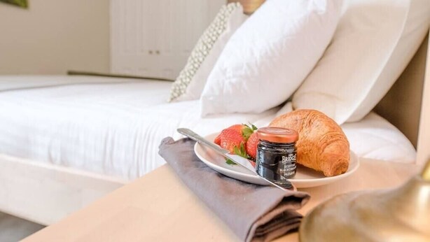 A neatly made bed with white linens, a plate with a croissant, strawberries, and a jar of chocolate spread. - No 12. Southwold (Southwold)
