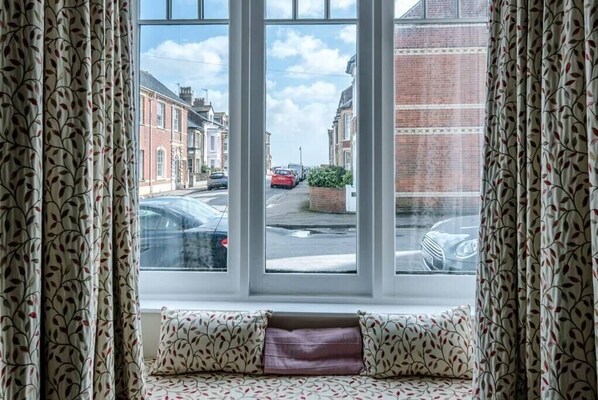Una habitación con un ventanal grande, un sofá estampado y vistas a una calle con coches aparcados y edificios.