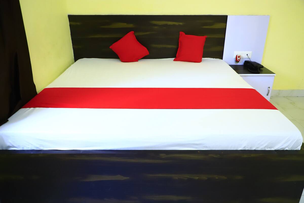 Una cama con una colcha roja y blanca, dos almohadas rojas y una mesita de noche con un teléfono.