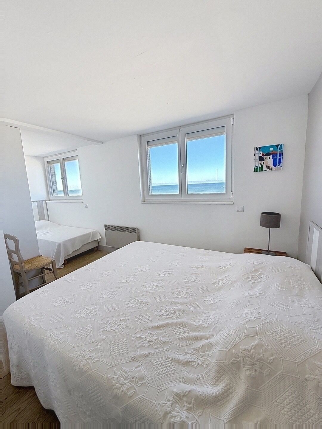 Un dormitorio con una cama grande, una silla, un escritorio y un ventanal con vistas al mar.