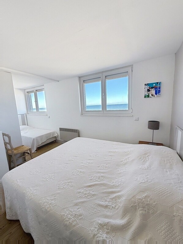 Un dormitorio con una cama grande, una silla, un escritorio y un ventanal con vistas al mar.