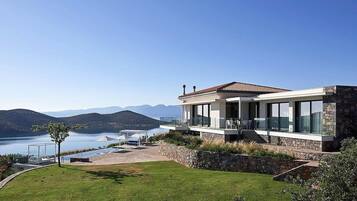 Une maison moderne avec une façade en pierre, de grandes fenêtres en verre et une vue sur un lac et des montagnes.