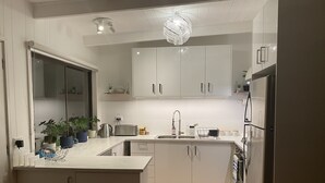 A modern kitchen with white cabinets, a marble countertop, a chandelier, and a built-in refrigerator. - Newly Renovated Hamptons-Style Beach House - Includes Linen & EV Charger! (Coronet Bay)