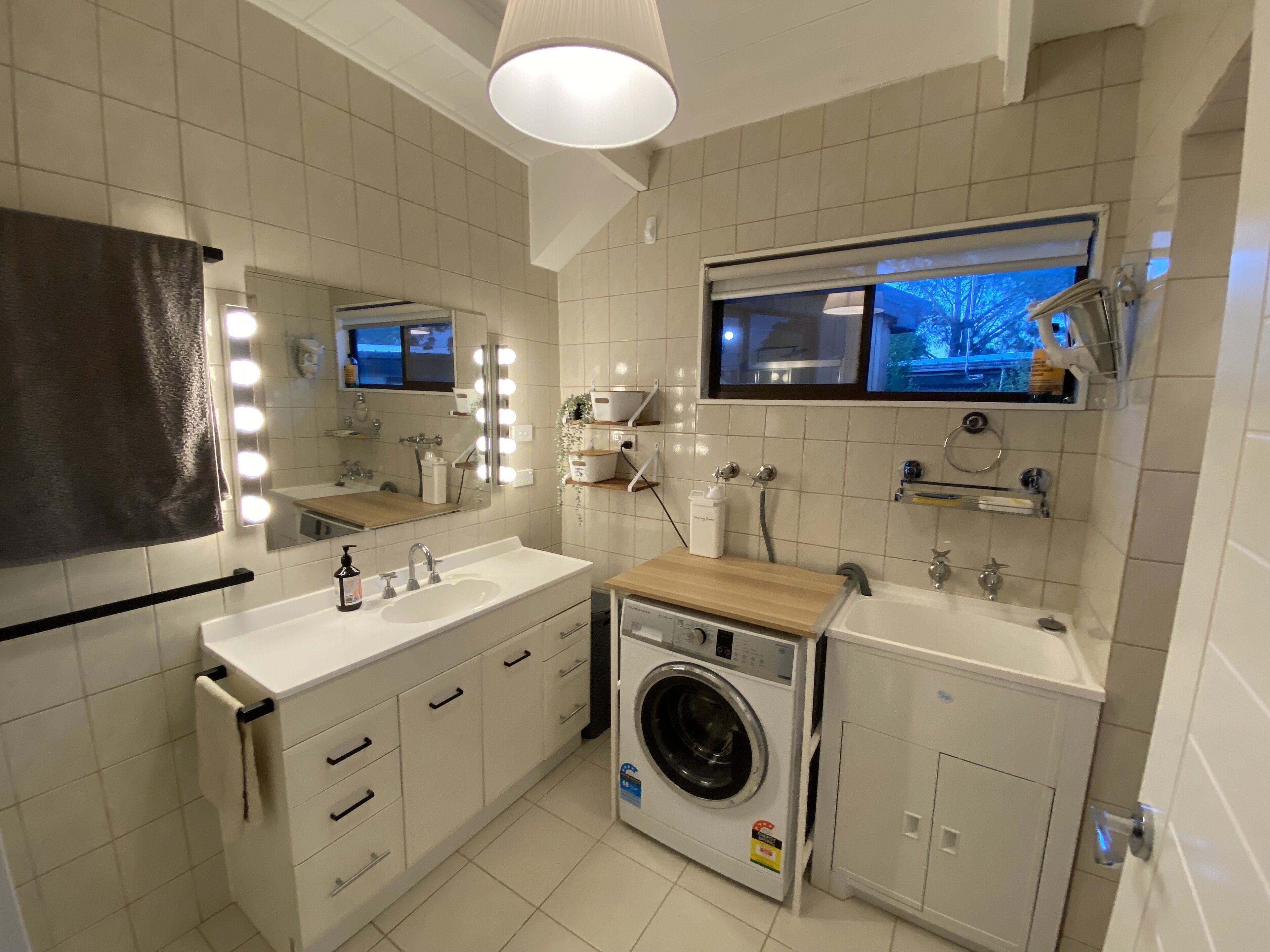 A modern bathroom with a large mirror, vanity, sink, and washing machine.
