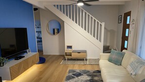 A modern living room with a flat-screen TV, a staircase, a white sofa, and a patterned rug. - Newly Renovated Hamptons-Style Beach House - Includes Linen & EV Charger! (Coronet Bay)