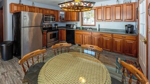 A kitchen with wooden cabinets, stainless steel appliances, a round table with chairs, and a stained glass light fixture.