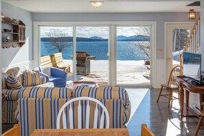 En stue med sofa, bord og fjernsyn. Stort vindue med udsigt over sø og bjerge.