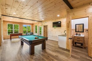 A wooden interior with a pool table, a TV, and a kitchenette.
