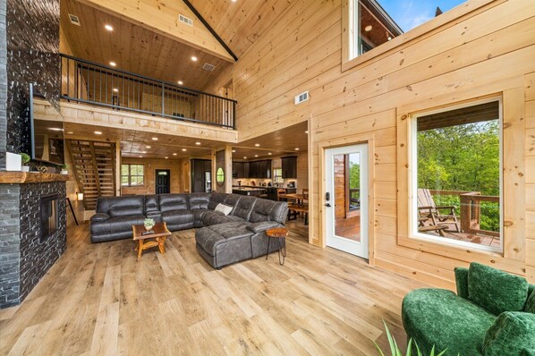 A spacious wooden cabin with a large living area, a kitchen, and a balcony with a view of the forest.