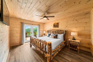 A wooden cabin bedroom with a bed, a ceiling fan, a nightstand, and a view through a glass door. - Spacious & Upscale with 7 Person Hot Tub, Theater, Views, Game Room, Sauna (Sevierville)