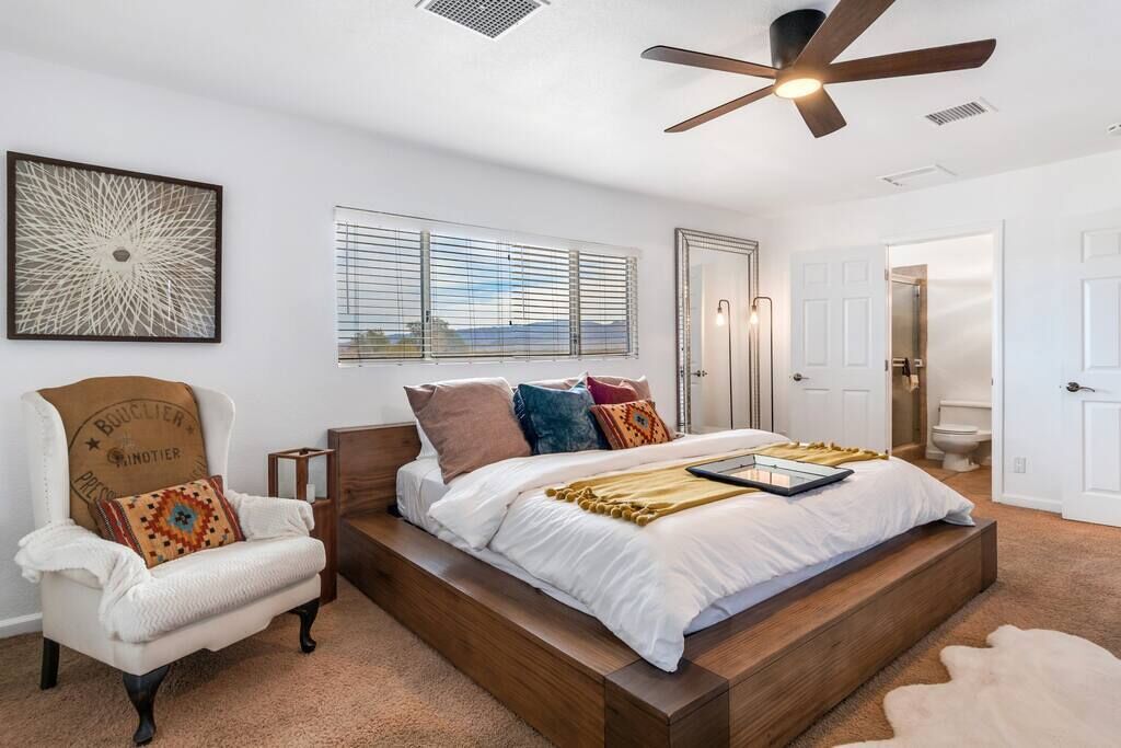 A bedroom with a large bed, a ceiling fan, a chair, and a window with blinds.