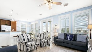 A spacious living room with striped armchairs, a dark sofa, and a view of the city through large windows.