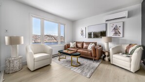 Una sala de estar moderna con un sofá de cuero, dos sillones, una mesa de centro y un ventanal que ofrece vistas a un paisaje nevado.