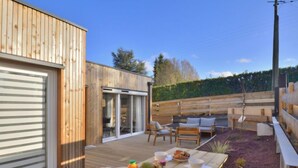 Une terrasse en bois avec une table préparée pour le petit-déjeuner, des sièges d’extérieur et une porte-fenêtre coulissante donnant sur un patio abrité.