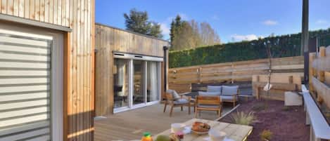 A wooden deck with a table set for breakfast, outdoor seating, and a sliding glass door leading to a covered patio.
