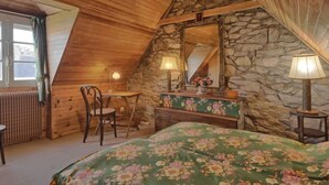 A cozy attic bedroom with wooden beams, a stone wall, a bed with floral bedding, a desk with a chair, and two lamps. - Ker Vignan by Interhome (Ile Grande)