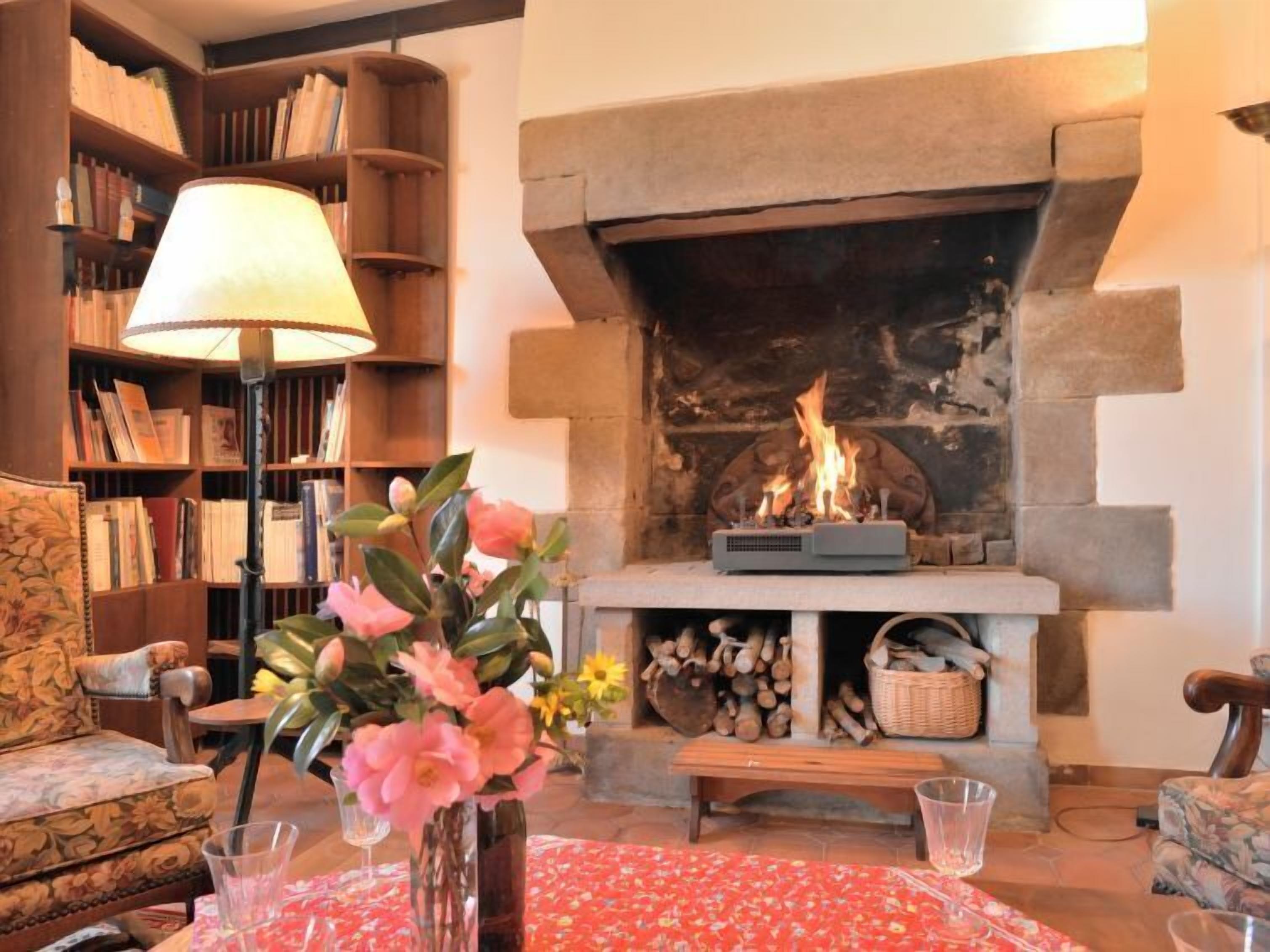 A cozy living room with a fireplace, bookshelves, a floral sofa, and a table with a vase of flowers.