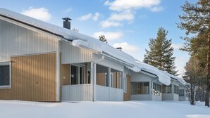 A row of cabins with large windows and a covered porch area, surrounded by snow.