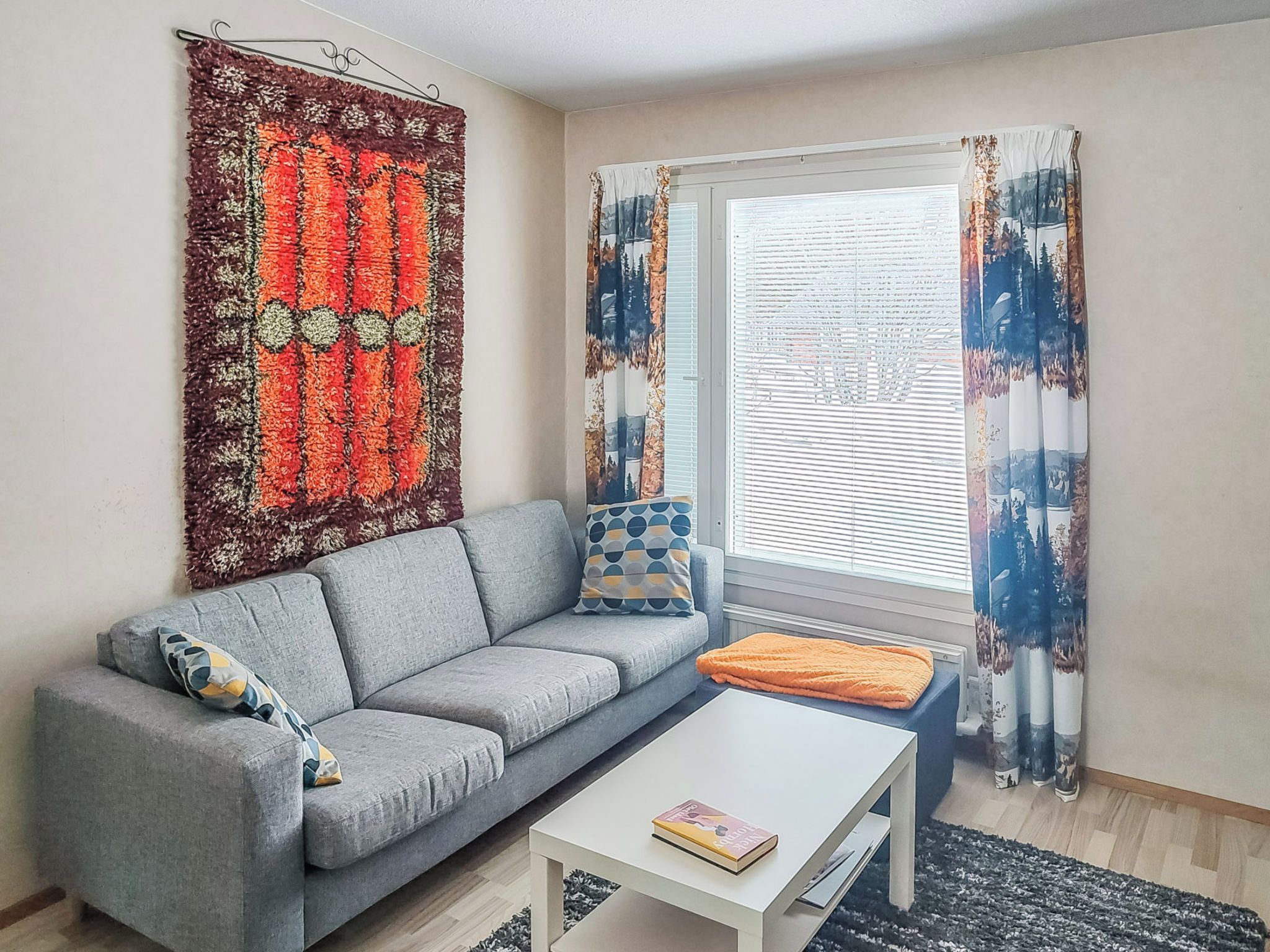 Una sala de estar con un sofá gris, una mesa de centro blanca y un tapete con estampado rojo y naranja.