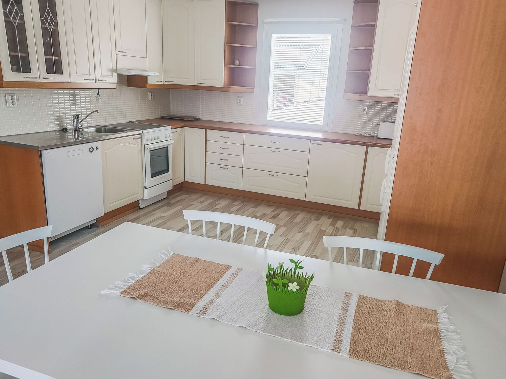 A kitchen with white cabinets, a white stove, a sink, and a window with blinds.