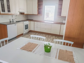 Une cuisine avec des meubles blancs, une cuisinière blanche, un évier et une fenêtre avec des stores.