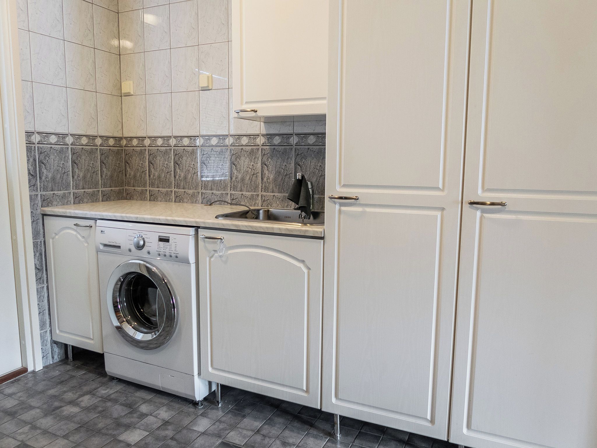 A laundry area with a washing machine, a sink, and cabinets.