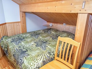 Una habitación pequeña con cama individual, colcha de estampado de cebra, una silla de madera y techo inclinado.