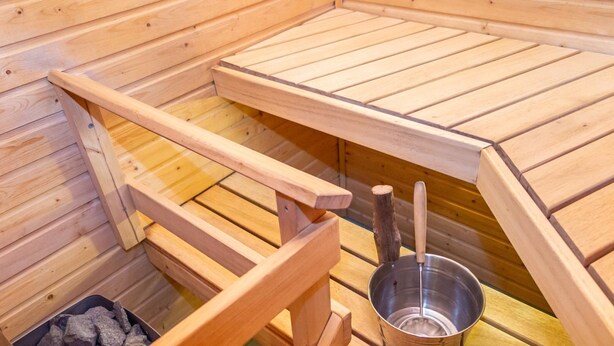 Una sauna con bancos de madera, una cuenca metálica y un recipiente con piedras.