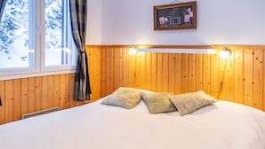 Una cama con cabecera de madera, una ventana con cortinas y una lámpara de pared.