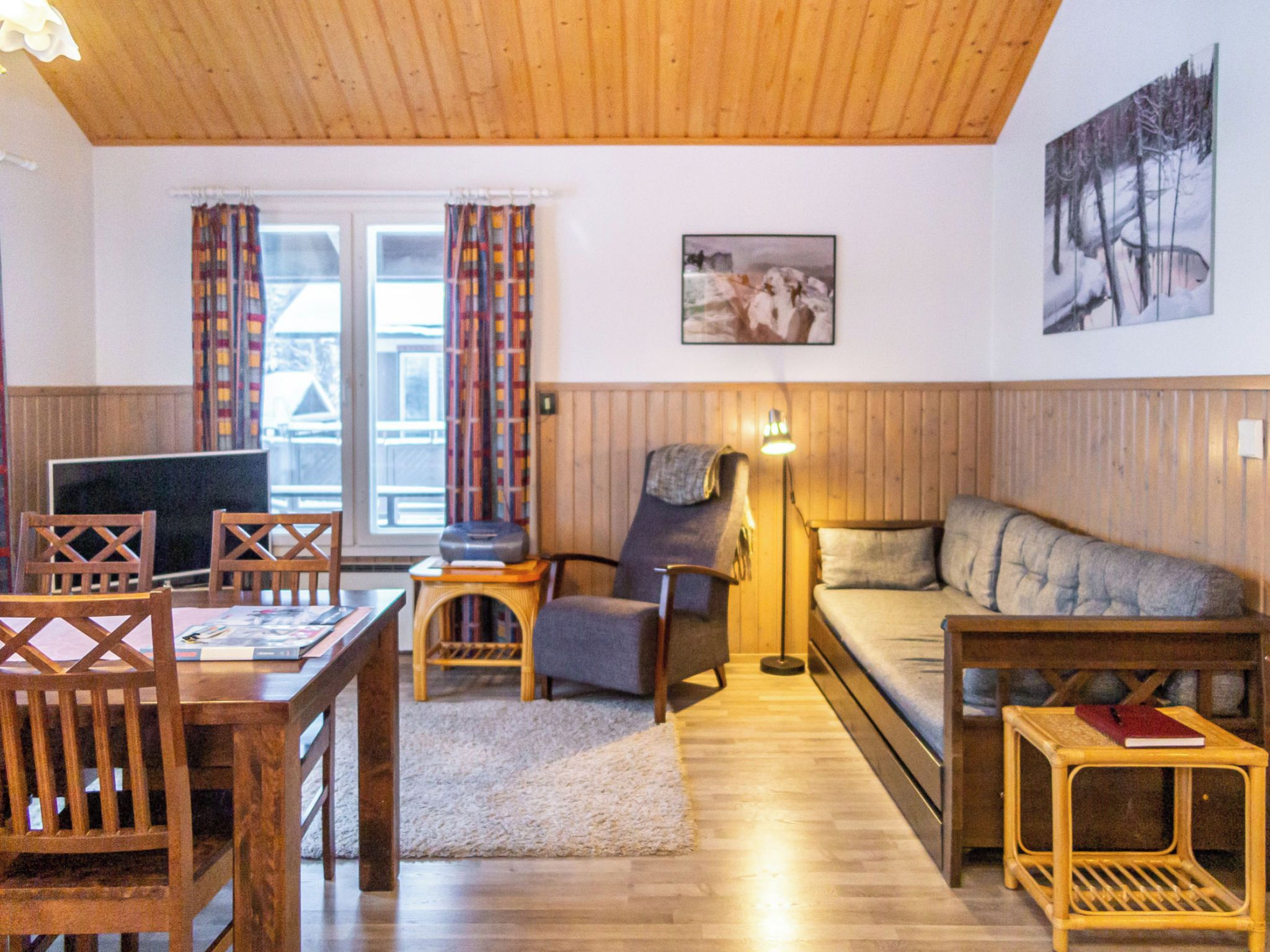 Ein gemütliches Wohnzimmer mit Holzboden, einer Couch, einem Esstisch mit Stühlen und einem Fernseher.