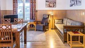 Una sala de estar acogedora con piso de madera, un sofá, un sillón, una mesa y un televisor.