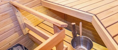 Eine Sauna mit Holzbänken, einem Metallbecken und einem Behälter mit Steinen.