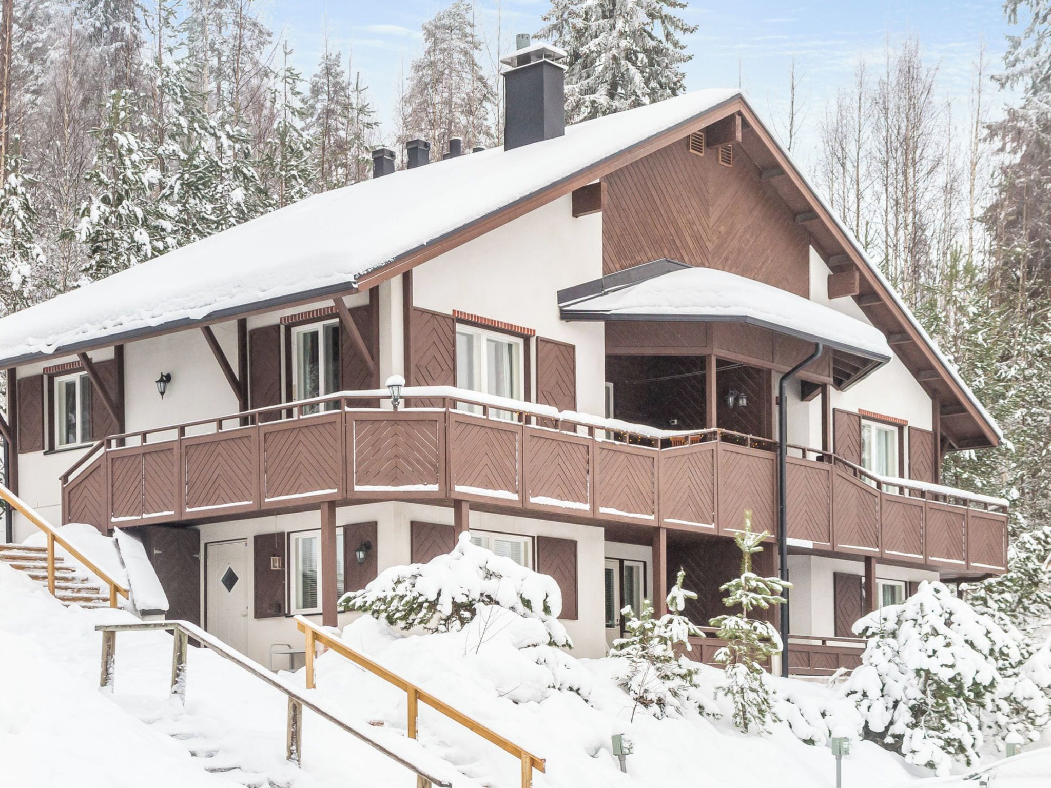 Een chalet met meerdere verdiepingen en een balkon, omgeven door met sneeuw bedekte bomen.