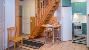 Una cocina con escalera de madera, un taburete de bar y un refrigerador.