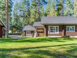 A cabin with a porch and a covered outdoor seating area, surrounded by a forest.