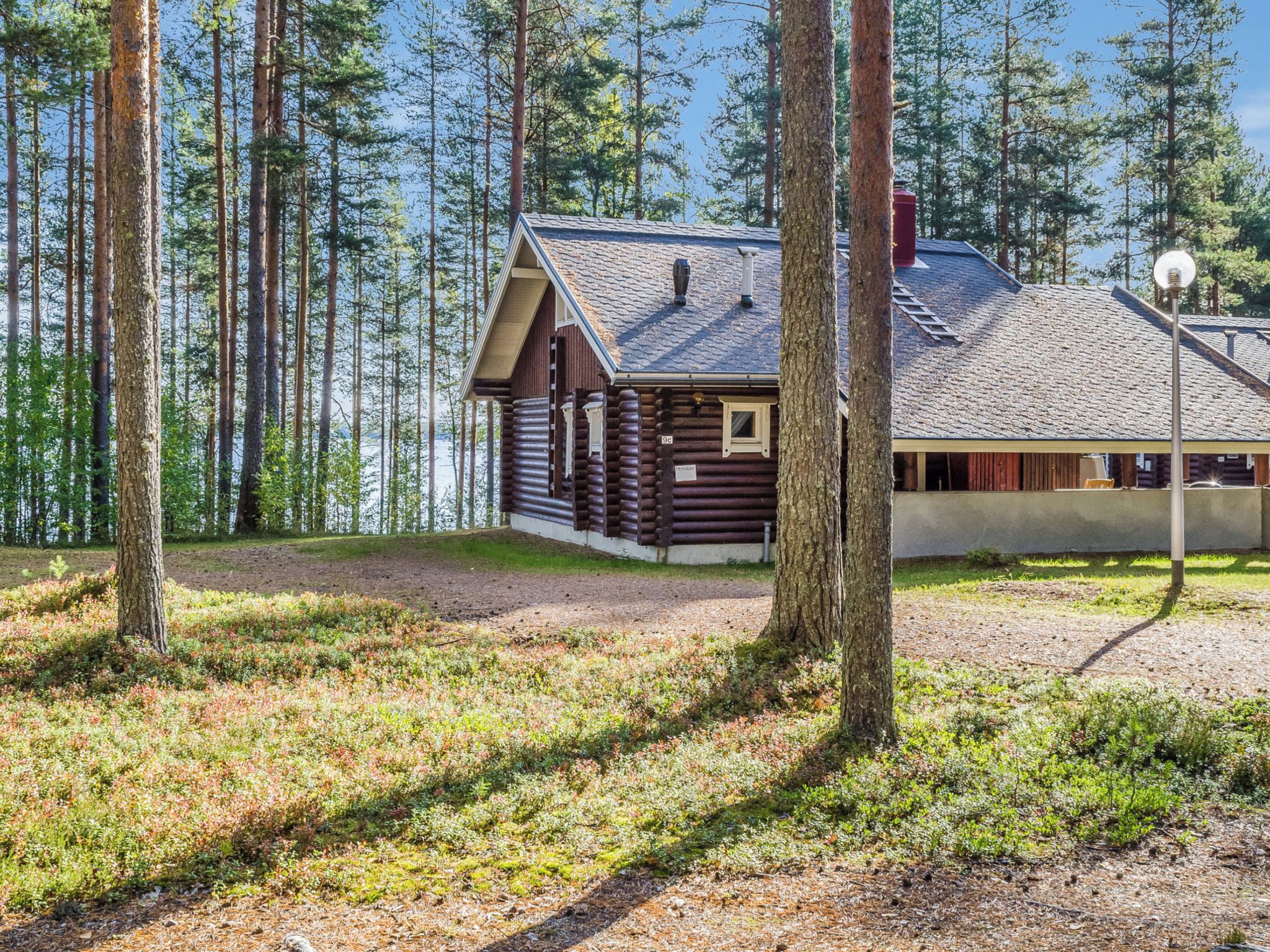 Eine Blockhütte mit Schornstein, umgeben von Wald und einem Gewässer.