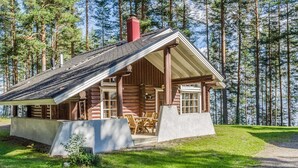 Una cabaña de troncos con un porche y zona de estar al aire libre, rodeada de un bosque.