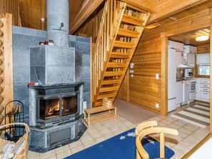 A cozy cabin interior with a stone fireplace, wooden staircase, and a kitchenette.