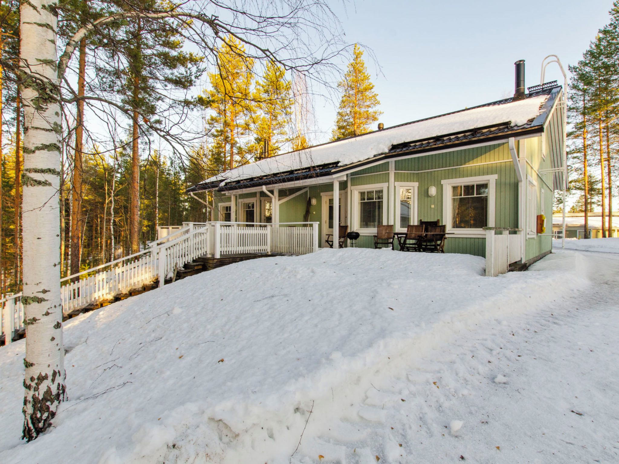 A green building with a white porch, a covered outdoor seating area, and a snow-covered landscape.