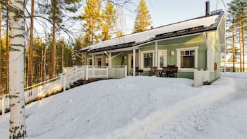 A green building with a white porch, a covered outdoor seating area, and a snow-covered landscape.