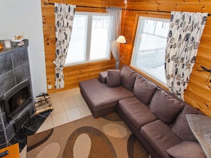 A cozy living room with a fireplace, a sectional sofa, and two windows with curtains.