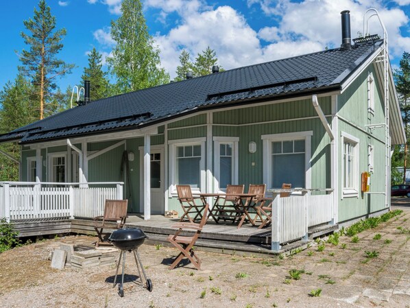 A green wooden building with a covered porch, outdoor seating, and a barbecue grill.